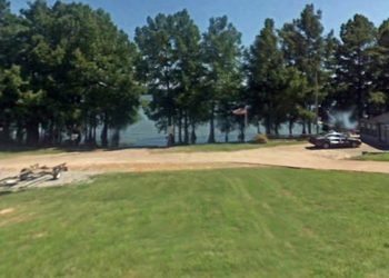 Green area with dirt road in front of trees and a lake during the day