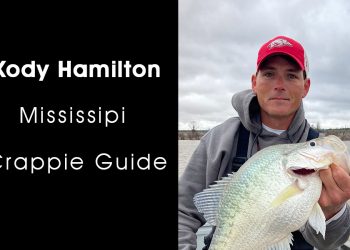 Man in grey jacket and bright red hat holding a crappie.