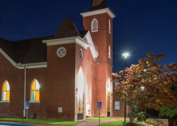 Brick church with a steeple and lights at nighttime. 