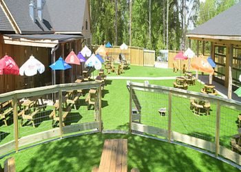 Outdoor green area with tables, chairs, benches, and umbrellas. 