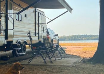 RV with an awning and dog overlooking the water on a bright day. 