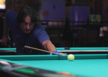 Man getting ready to hit a pool ball on a green pool table in a dark room